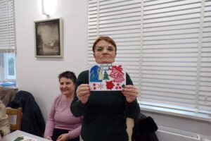 Mieszkańcy i personel Domu Pomocy Społecznej w Lubzinie pozują do grupowego zdjęcia, dumnie prezentując ręcznie robione kartki świąteczne wykonane podczas warsztatów.