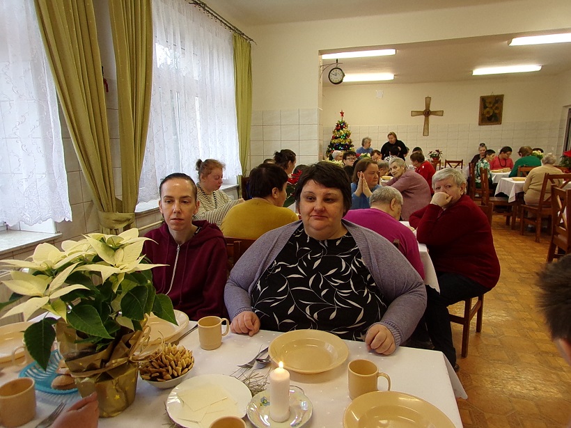 Mieszkańcy Domu Pomocy Społecznej w Lubzinie siedzą przy wspólnym stole podczas świątecznego posiłku. Na stole stoi biała gwiazda betlejemska, w tle widoczna jest choinka.